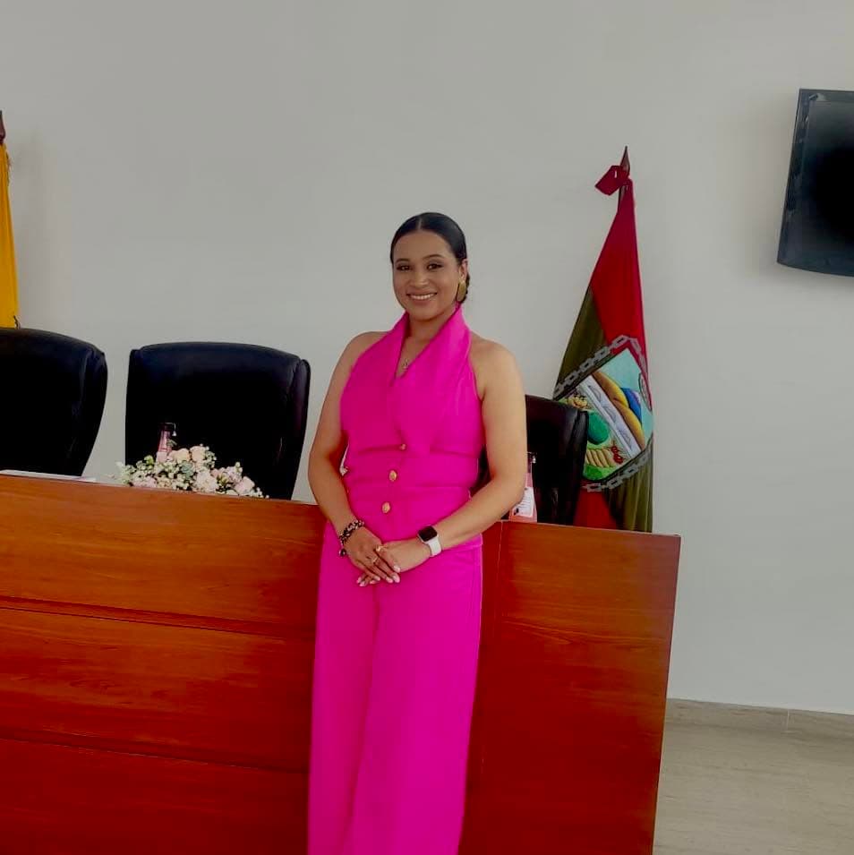 Helen de pie en un salón de sesiones, junto a la bandera de Píllaro